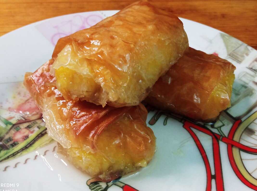 Ατομικά γαλακτομπουρεκάκια σε πιάτο, σιροπιασμένα και τραγανά, με φλούδα πορτοκαλιού.