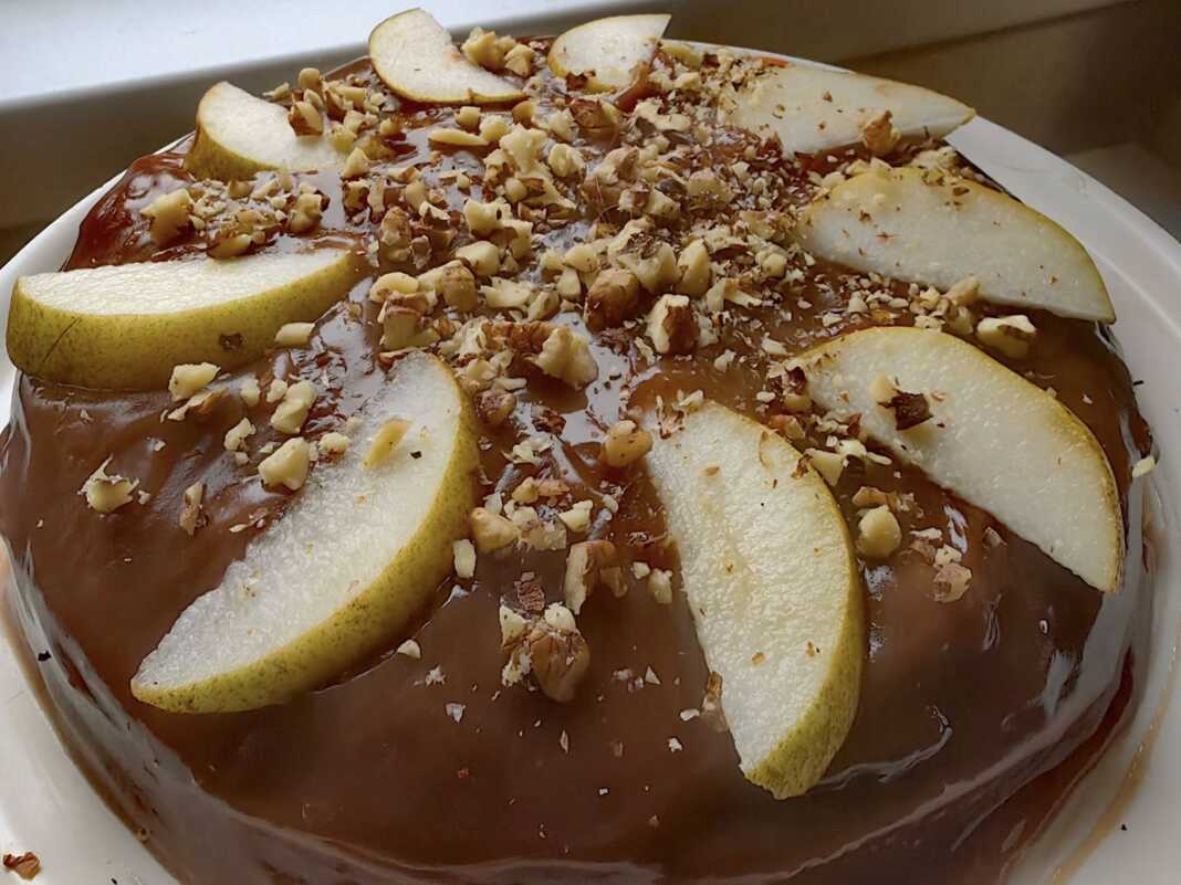 keik sokolata axladia Ένα κομμάτι λαχταριστού κέικ σοκολάτας με φέτες αχλαδιού στην επιφάνεια.