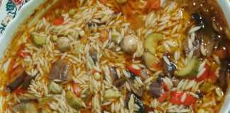 Ένα ταψί με γιουβέτσι λαχανικών, όπου διακρίνονται το κριθαράκι και τα πολύχρωμα λαχανικά σε κόκκινη σάλτσα.