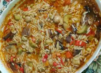 Ένα ταψί με γιουβέτσι λαχανικών, όπου διακρίνονται το κριθαράκι και τα πολύχρωμα λαχανικά σε κόκκινη σάλτσα.