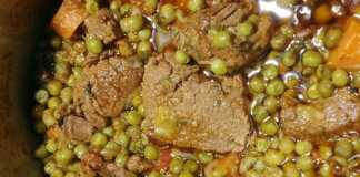 Μία κατσαρολα με μοσχαράκι κοκκινιστό, πράσινο αρακά και πορτοκαλί καρότα σερβιρισμένο σε βαθύ πιάτο.