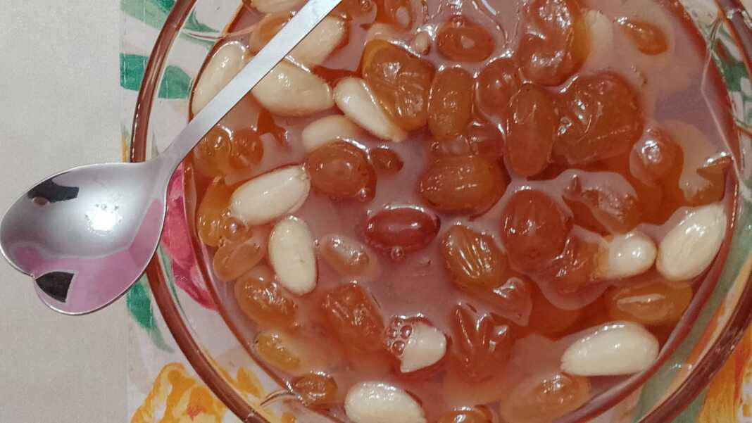 Γλυκό σταφύλι σε ένα μπολ, με τις ρώγες να γυαλίζουν στο σιρόπι και λίγα αμύγδαλα.