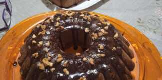 Ένα νηστίσιμο κέικ πορτοκαλιού με γλάσο σοκολάτας και πασπαλισμένα καρύδια σε μια πιατέλα.