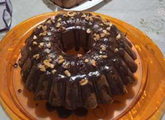 Ένα νηστίσιμο κέικ πορτοκαλιού με γλάσο σοκολάτας και πασπαλισμένα καρύδια σε μια πιατέλα.