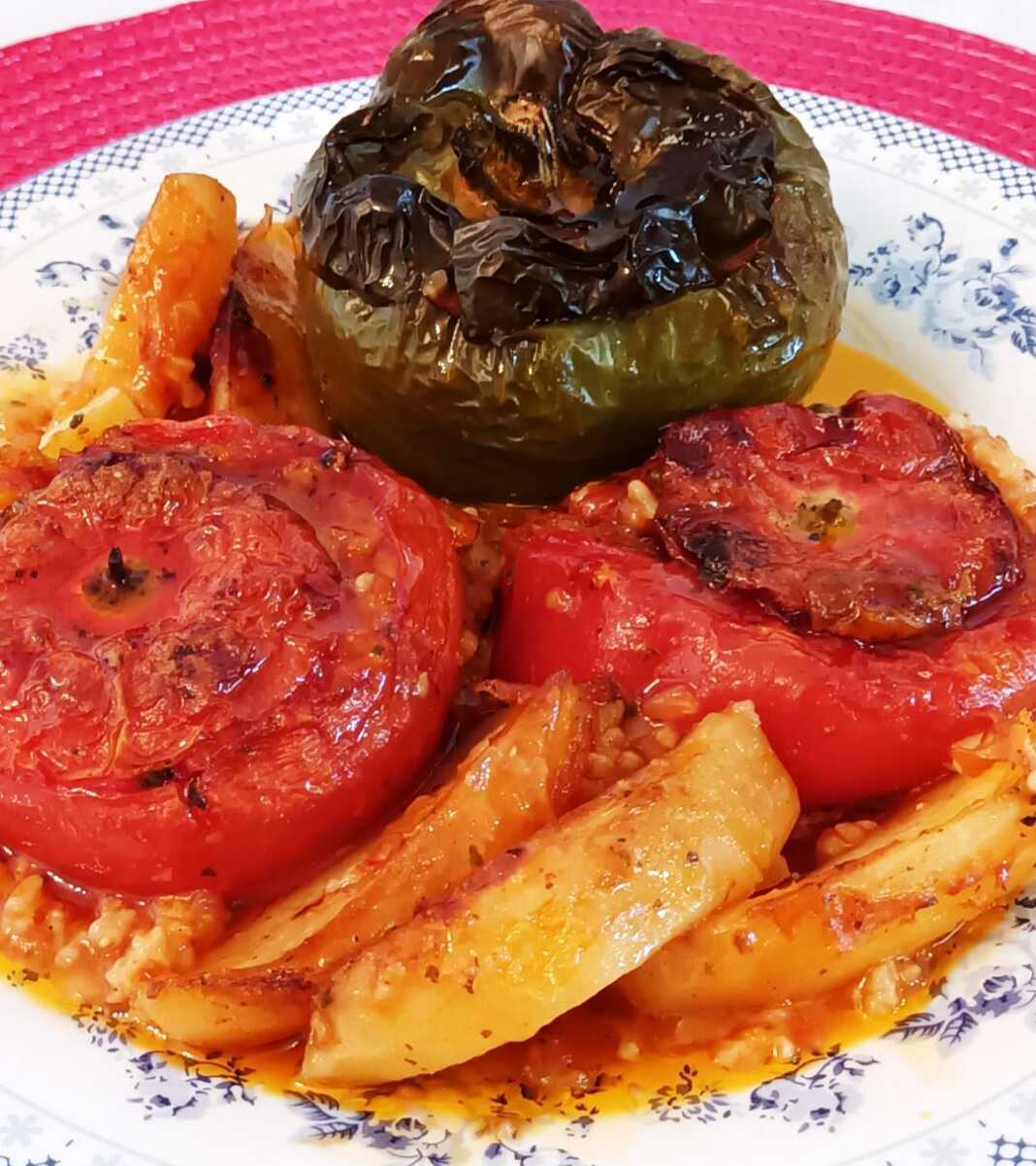 Ένα ταψί με γεμιστές ντομάτες, πιπεριές και μελιτζάνες, ανάμεσα σε κομμένες πατάτες.