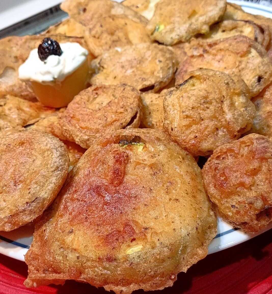 Ένα πιάτο με χρυσαφένια, τραγανά τηγανητά κολοκυθάκια και ένα μπολάκι με λευκή σως γιαουρτιού.