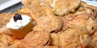 Ένα πιάτο με χρυσαφένια, τραγανά τηγανητά κολοκυθάκια και ένα μπολάκι με λευκή σως γιαουρτιού.