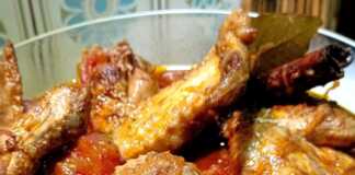 Κοτόπουλο κοκκινιστό με φτερούγες σε πιάτο, περιχυμένο με κόκκινη σάλτσα ντομάτας.