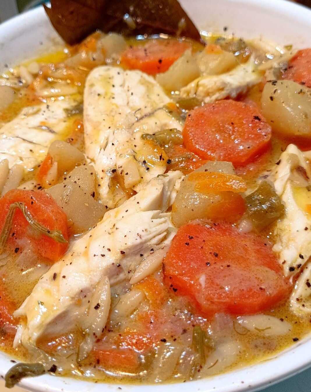 psarosoupa_lpu Πιάτο με ζεστή ψαρόσουπα λαβράκι, γεμάτη λαχανικά και κομμάτια ψαριού, γαρνιρισμένη με φρέσκα μυρωδικά σε ξύλινο τραπέζι.