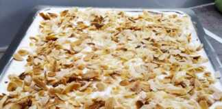 Μια στρωματοποιημένη τούρτα αμυγδάλου με λευκή κρέμα, πασπαλισμένη με αμύγδαλα φιλέ.