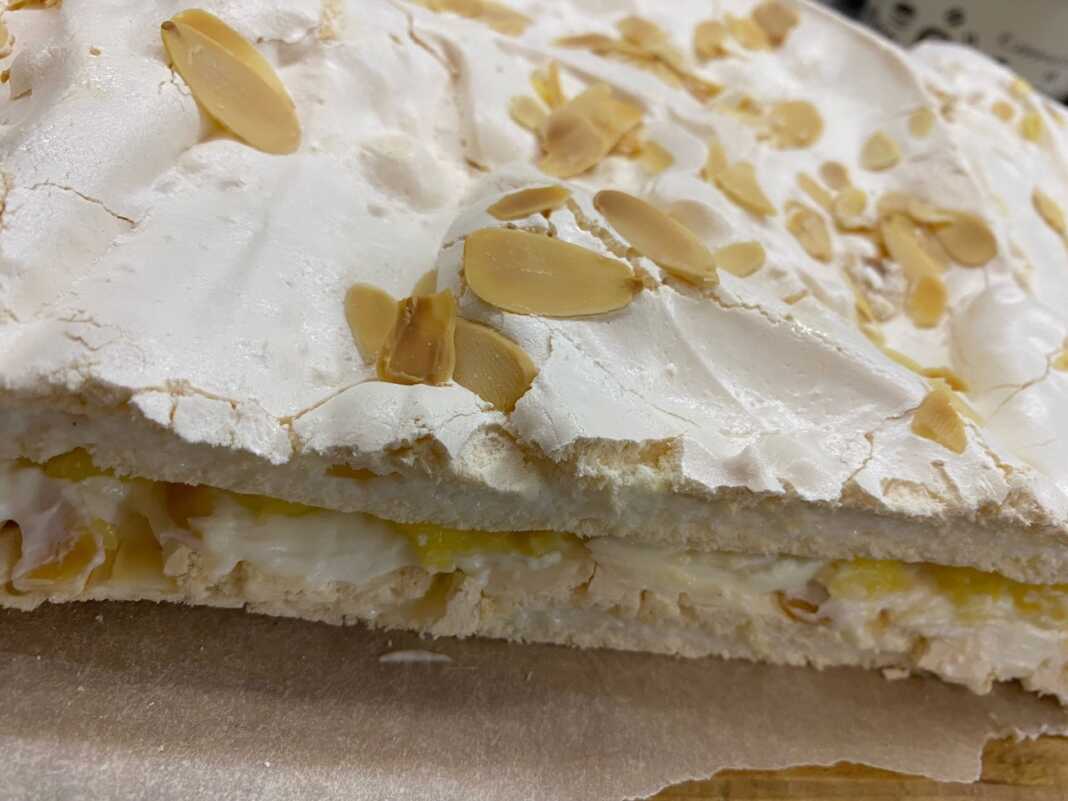 torta maregkati Μια στρωτή τούρτα μαρέγκας με εμφανή τα στρώματα λευκής μαρέγκας, κίτρινης κρέμας λεμονιού και λευκής κρέμας μασκαρπόνε.