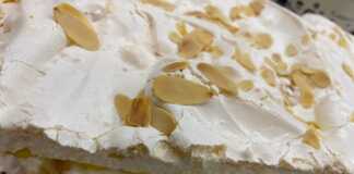 Μια στρωτή τούρτα μαρέγκας με εμφανή τα στρώματα λευκής μαρέγκας, κίτρινης κρέμας λεμονιού και λευκής κρέμας μασκαρπόνε.