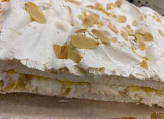 Μια στρωτή τούρτα μαρέγκας με εμφανή τα στρώματα λευκής μαρέγκας, κίτρινης κρέμας λεμονιού και λευκής κρέμας μασκαρπόνε.