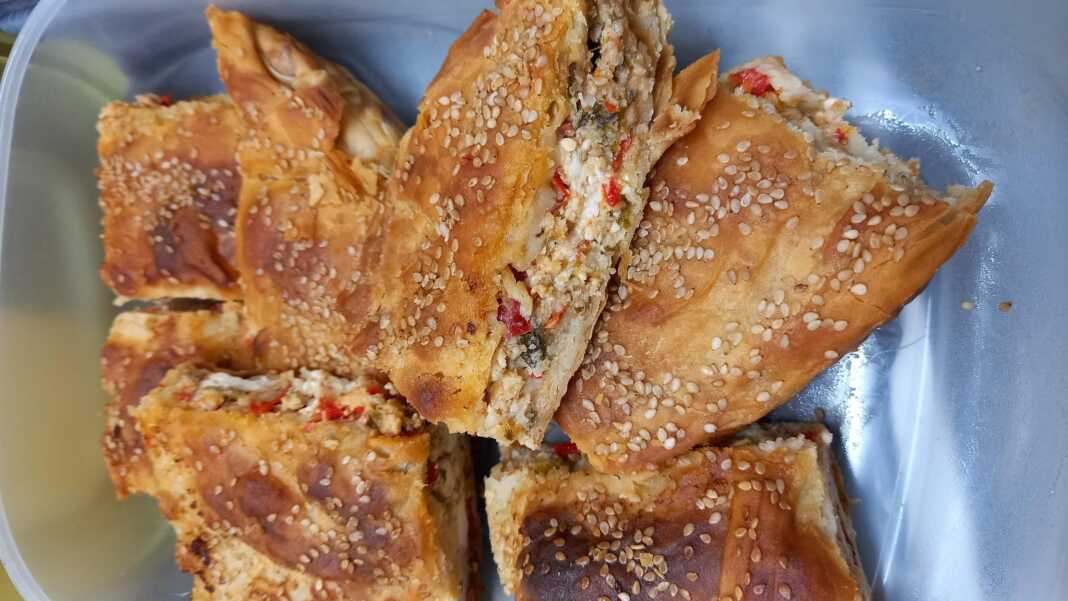 Μια χρυσαφένια, ψημένη πιπερόπιτα κομμένη σε κομμάτια, που φαίνεται η λαχταριστή γέμιση με τα χρωματιστά λαχανικά και το τυρί.