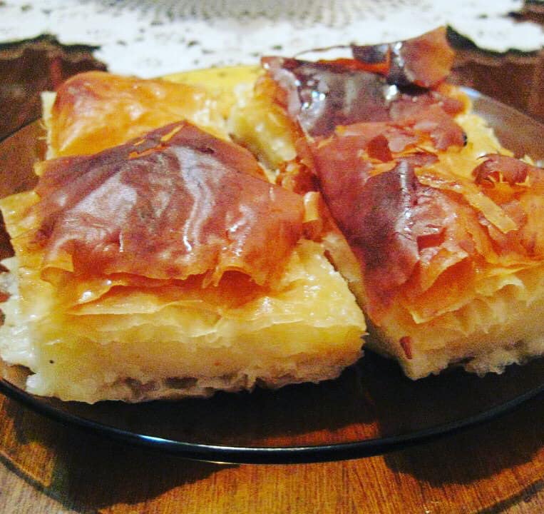 galaktompoureko-lop Φρέσκο, χρυσαφένιο σπιτικό γαλακτομπούρεκο κομμένο σε τετράγωνα κομμάτια, με το σιρόπι να γυαλίζει στην επιφάνεια.