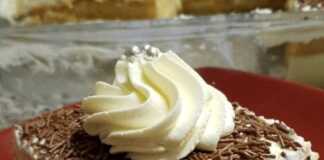 Ένα κομμάτι γλυκού σε ένα πιάτο, με στρώσεις από σιροπιασμένες φρυγανιές, μια παχιά στρώση κίτρινης κρέμας και λευκή σαντιγί στην κορυφή, πασπαλισμένο με κανέλα.