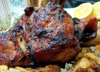 Ένα χοιρινό κότσι ψημένο στο φούρνο με σκούρα μπύρα, με τραγανή καφέ πετσούλα, σε ένα βαθύ σκεύος. Δίπλα διακρίνονται ψημένες, σπασμένες πατάτες.