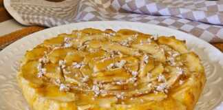 Ένα στρογγυλό κέικ μήλου με φέτες μήλου στην επιφάνεια πασπαλισμένο με άχνη ζάχαρη.