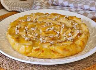 Ένα στρογγυλό κέικ μήλου με φέτες μήλου στην επιφάνεια πασπαλισμένο με άχνη ζάχαρη.