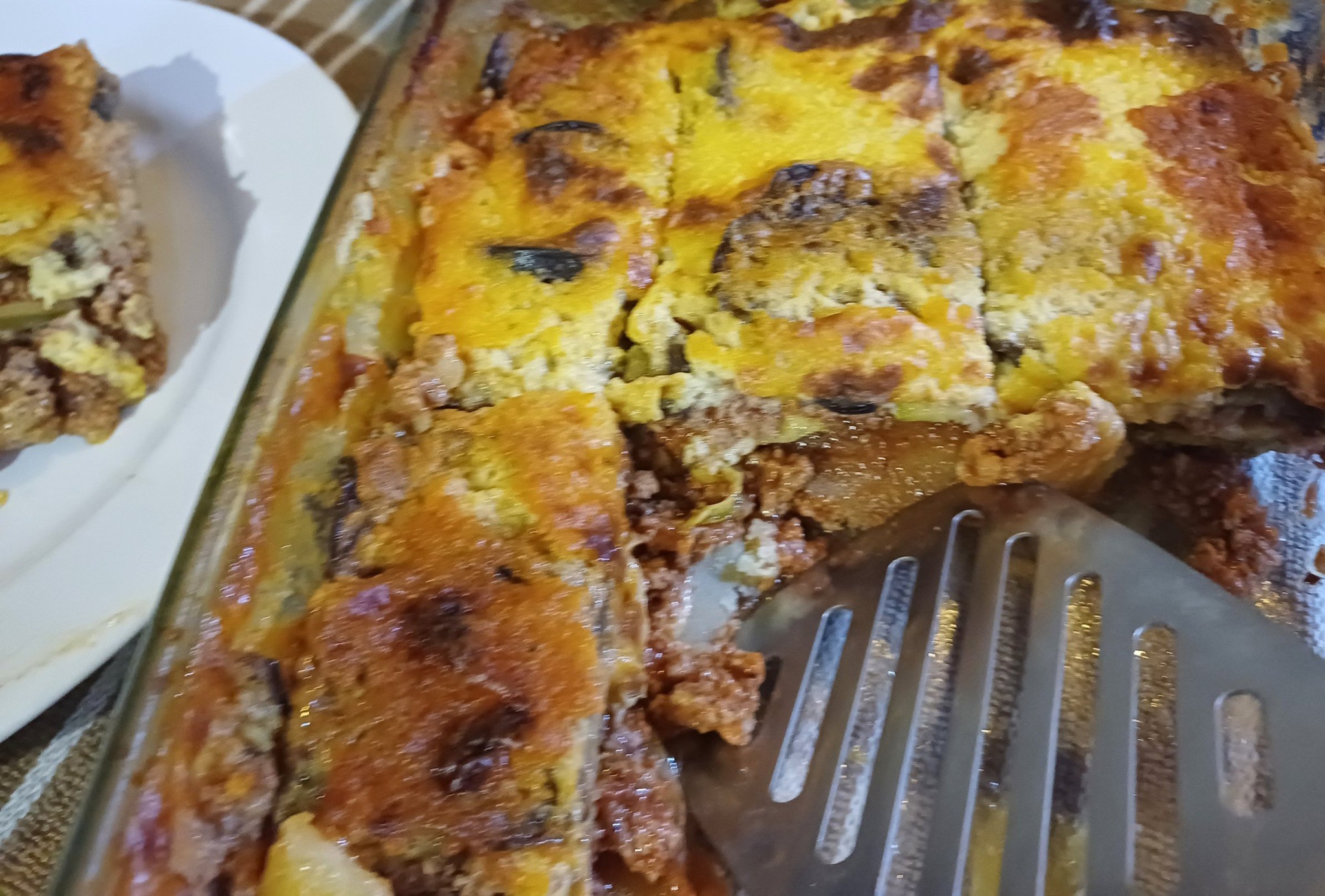 Ένα ταψί με χρυσαφένιο μουσακά, όπου διακρίνονται οι στρώσεις λαχανικών και κιμά, με μια παχιά κρούστα μπεσαμέλ από πάνω.