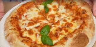 Μια στρογγυλή ναπολιτάνικη πίτσα με κόκκινη σάλτσα ντομάτας, λευκή μοτσαρέλα και πράσινα φύλλα βασιλικού. Η κόρα είναι φουσκωτή και ελαφρώς καμένη.