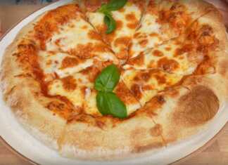 Μια στρογγυλή ναπολιτάνικη πίτσα με κόκκινη σάλτσα ντομάτας, λευκή μοτσαρέλα και πράσινα φύλλα βασιλικού. Η κόρα είναι φουσκωτή και ελαφρώς καμένη.