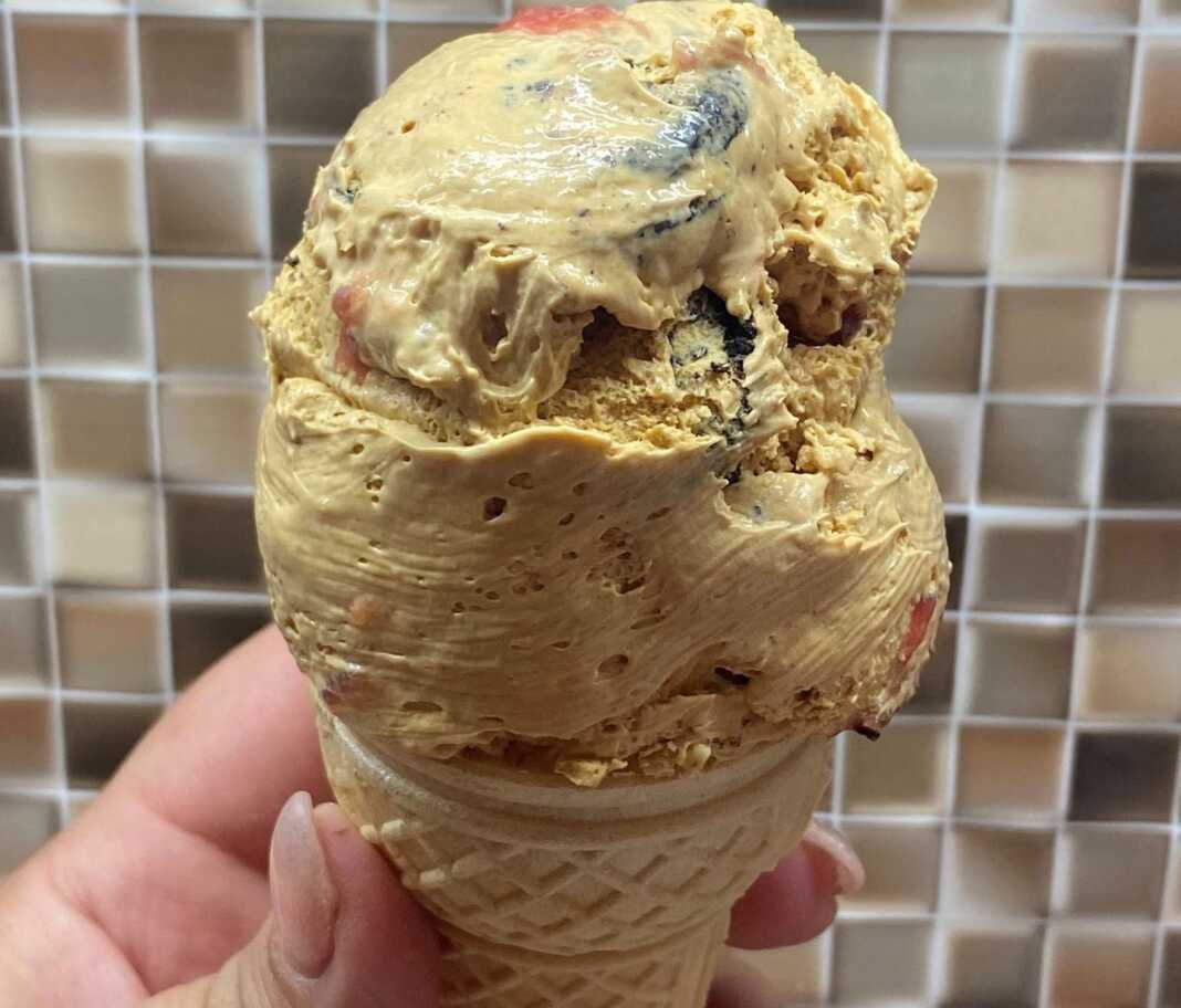 Ένα μπολ με σπιτικό παγωτό με κομματάκια μπισκότου και σάλτσα φράουλας, δίπλα σε χωνάκια βάφλας.