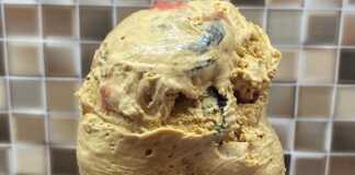 Ένα μπολ με σπιτικό παγωτό με κομματάκια μπισκότου και σάλτσα φράουλας, δίπλα σε χωνάκια βάφλας.