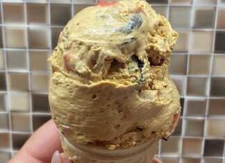 Ένα μπολ με σπιτικό παγωτό με κομματάκια μπισκότου και σάλτσα φράουλας, δίπλα σε χωνάκια βάφλας.