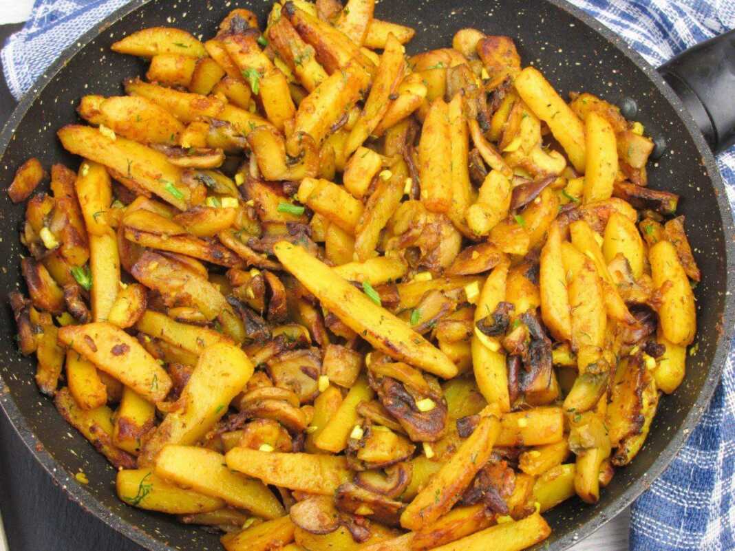 Ένα τηγάνι με χρυσαφένιες τηγανητές πατάτες ανακατεμένες με σωταρισμένα μανιτάρια και φέτες κρεμμυδιού.