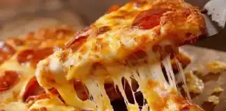 Σπιτική πίτσα έτοιμη για ψήσιμο, με απλωμένη σάλτσα ντομάτας, φέτες ζαμπόν, πιπεριές και τριμμένη μοτσαρέλα πάνω σε λεπτή ζύμη.