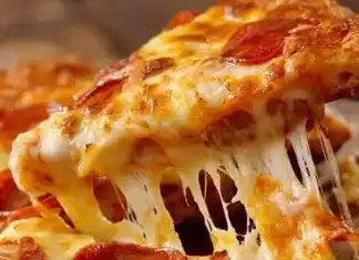 Πίτσα στο λεπτό Σπιτική πίτσα έτοιμη για ψήσιμο, με απλωμένη σάλτσα ντομάτας, φέτες ζαμπόν, πιπεριές και τριμμένη μοτσαρέλα πάνω σε λεπτή ζύμη.