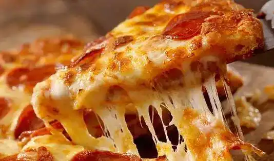 Σπιτική πίτσα έτοιμη για ψήσιμο, με απλωμένη σάλτσα ντομάτας, φέτες ζαμπόν, πιπεριές και τριμμένη μοτσαρέλα πάνω σε λεπτή ζύμη.