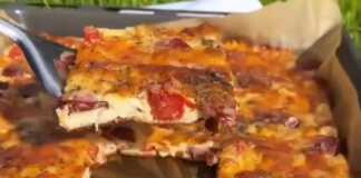 Μια σπιτική πίτσα με ζύμη γιαουρτιού, με διάφορα λαχανικά, λουκάνικο και λιωμένο τυρί, σε ένα ταψί.