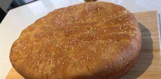 Ένα στρογγυλό ζυμωτό ψωμί μέσα σε μια πήλινη γάστρα, πασπαλισμένο με σουσάμι.