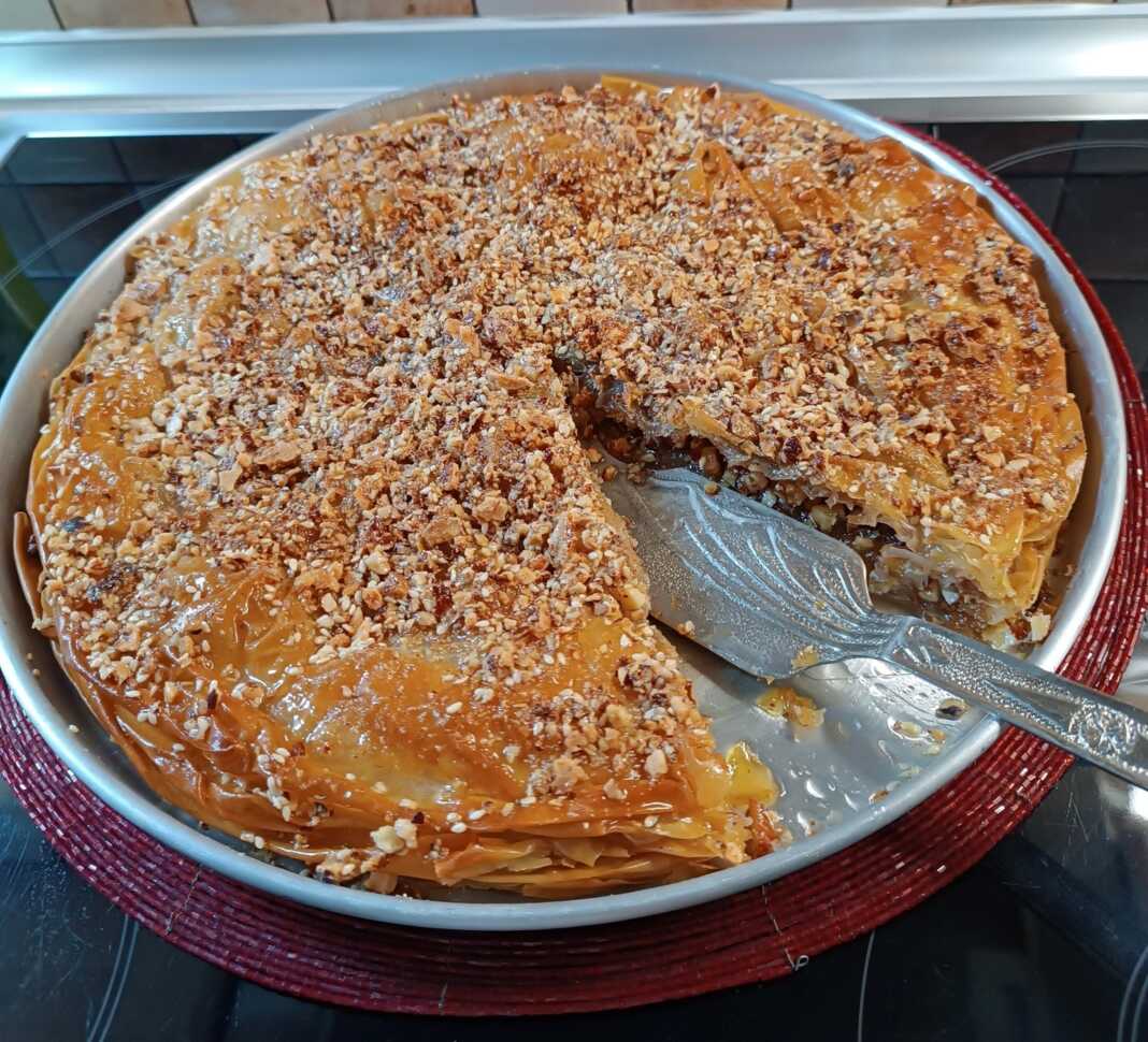 Τάρτα μπακλαβάς μόλις σιροπιάστηκε, με εμφανείς τις χαραγμένες μερίδες και πασπαλισμένους ξηρούς καρπούς.