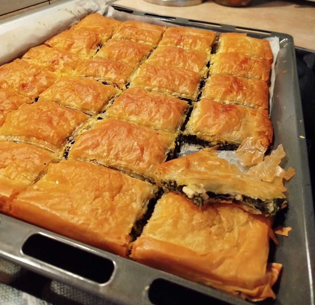 Μια χρυσαφένια σπανακοτυρόπιτα κομμένη σε μερίδες σε ένα ταψί.