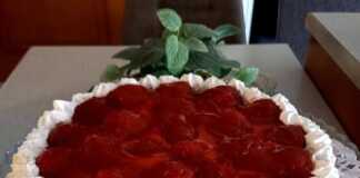 Μια στρογγυλή τάρτα φράουλας με χρυσαφένιο παντεσπάνι, στρώση λευκής σαντιγί, φρέσκες κόκκινες φράουλες τοποθετημένες κυκλικά και γυαλιστερό κόκκινο ζελέ από πάνω.