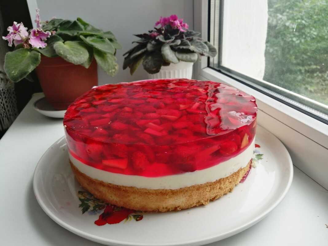 Μια στρογγυλή τούρτα με στρώσεις από παντεσπάνι, λευκή κρέμα και κόκκινες φράουλες σε διάφανο ζελέ στην κορυφή.