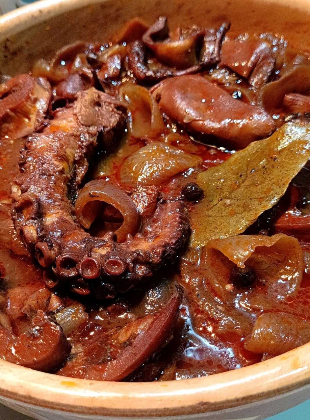 xtapodi karamelomeno krasato Ένα πήλινο σκεύος γεμάτο με χταπόδι κρασάτο, με κόκκινη σάλτσα, κρεμμύδια και μυρωδικά.