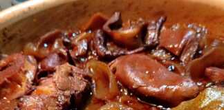 Ένα πήλινο σκεύος γεμάτο με χταπόδι κρασάτο, με κόκκινη σάλτσα, κρεμμύδια και μυρωδικά.