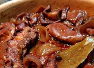 Ένα πήλινο σκεύος γεμάτο με χταπόδι κρασάτο, με κόκκινη σάλτσα, κρεμμύδια και μυρωδικά.