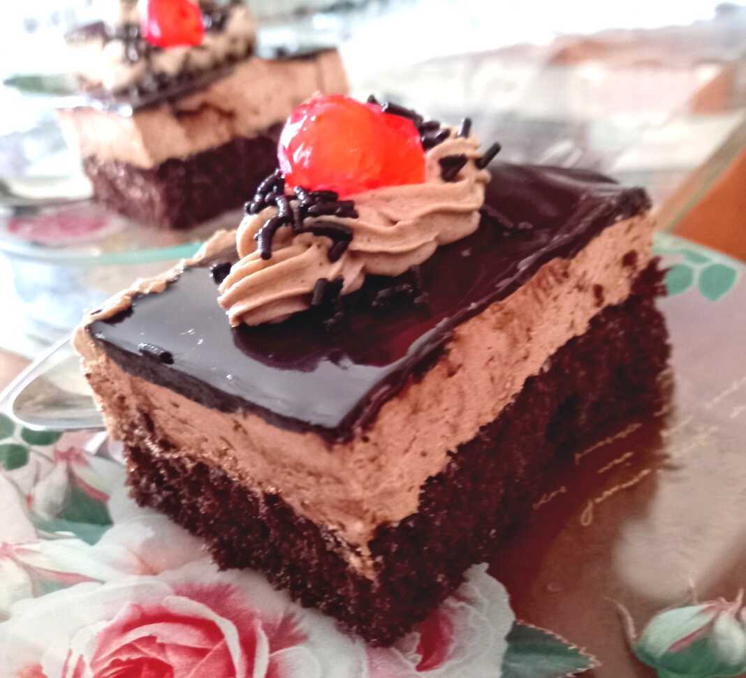 Ένα κομμάτι παστούλας ταψιού με στρώσεις παντεσπανιού σοκολάτας, κρέμας και γλάσου σοκολάτας.