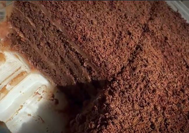 Keik sokolatas xoris psisimo Ένα ταψί κέικ σοκολάτας χωρίς ψήσιμο σε ένα πιάτο, που δείχνει τις στρώσεις από μπισκότα και κρέμα σοκολάτας, πασπαλισμένο με σοκολάτα.