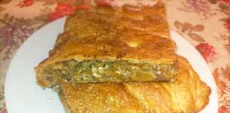 Ένα κομμάτι χρυσαφένιας, τραγανής κολοκυθόπιτας με εμφανή τη γέμιση λαχανικών και τυριών, τοποθετημένο σε ξύλινη επιφάνεια.