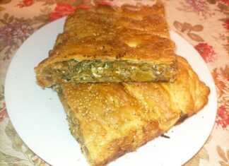 Κολοκυθόπιτα με Λαχανικά και Τυριά Ένα κομμάτι χρυσαφένιας, τραγανής κολοκυθόπιτας με εμφανή τη γέμιση λαχανικών και τυριών, τοποθετημένο σε ξύλινη επιφάνεια.