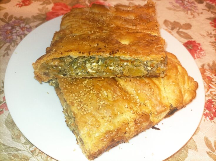 Ένα κομμάτι χρυσαφένιας, τραγανής κολοκυθόπιτας με εμφανή τη γέμιση λαχανικών και τυριών, τοποθετημένο σε ξύλινη επιφάνεια.