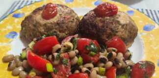 Δύο μπιφτέκια γεμιστά με τυρί σε ένα ταψί με λαδόκολλα, δίπλα σε ένα μπολ με σαλάτα από μαυρομάτικα φασόλια και κόκκινα ντοματίνια.