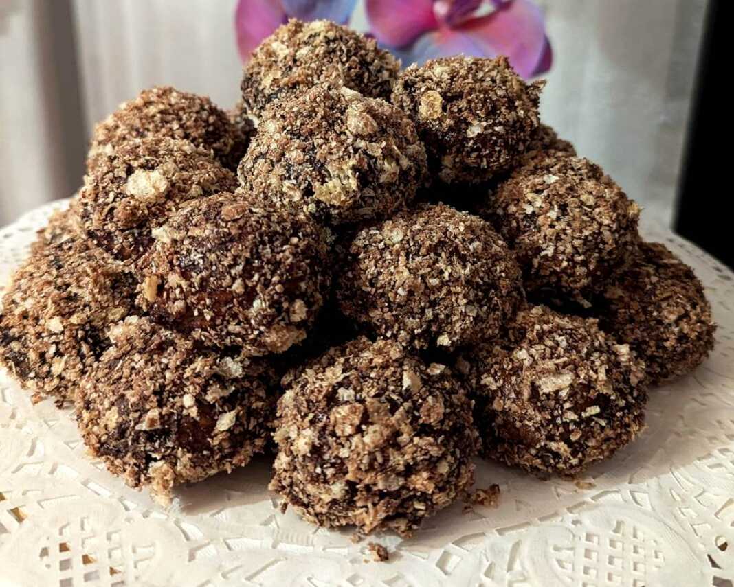 Μια πιατέλα γεμάτη μικρά, στρογγυλά μπισκότα καλυμμένα με σκούρο γλάσο σοκολάτας και τριμμένη ανοιχτόχρωμη γκοφρέτα.