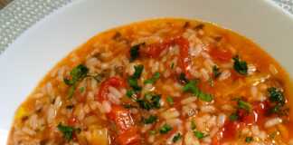 Ένα πιάτο με ζεστό, κοκκινωπό ντοματόρυζο, πασπαλισμένο με ψιλοκομμένο πράσινο μαϊντανό, έτοιμο για σερβίρισμα.